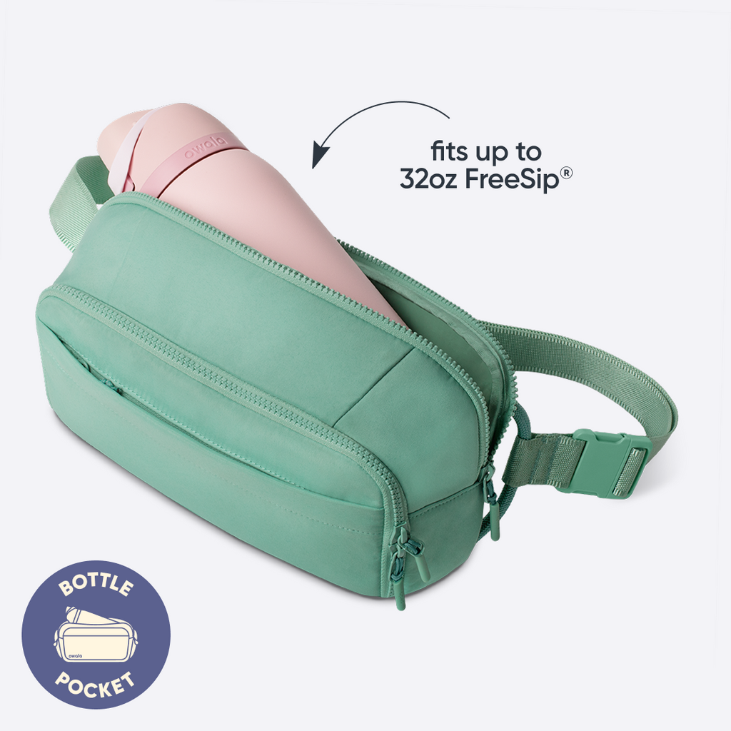 Owala All-Day Crossbody in Sea Glass, mint green nylon belt bag interior with a pink FreeSip bottle tucked inside, with badge reading "BOTTLE POCKET" and text overlay reading "fits up to 32oz FreeSip"