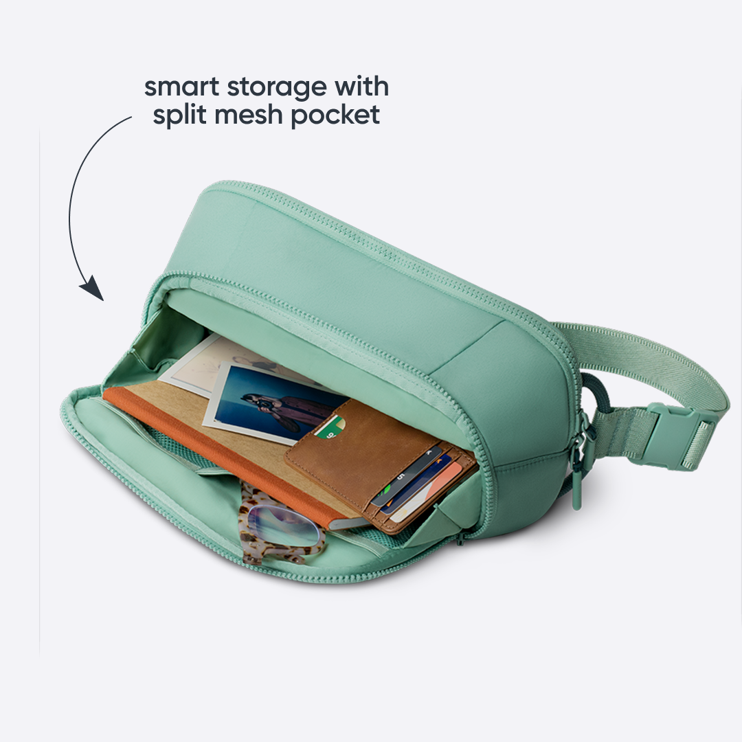 Owala All-Day Crossbody in Sea Glass, sage green ripstop body unzipped to show internal split mesh pocket holding cards, a wallet, and a phone, with text reading "smart storage with split mesh pocket"