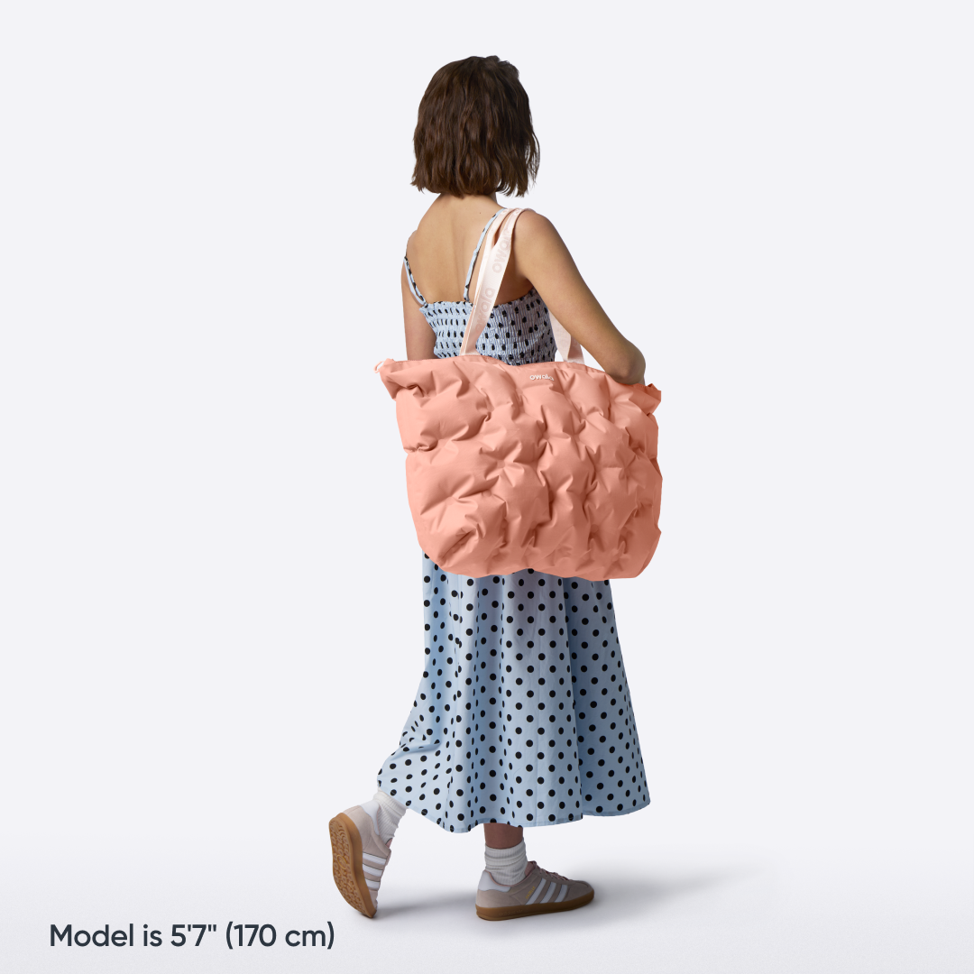 Model walking with the Owala Cloud tote in Rosewood slung over her shoulder, coral pink puffer-quilted body with blush owala-tape handles