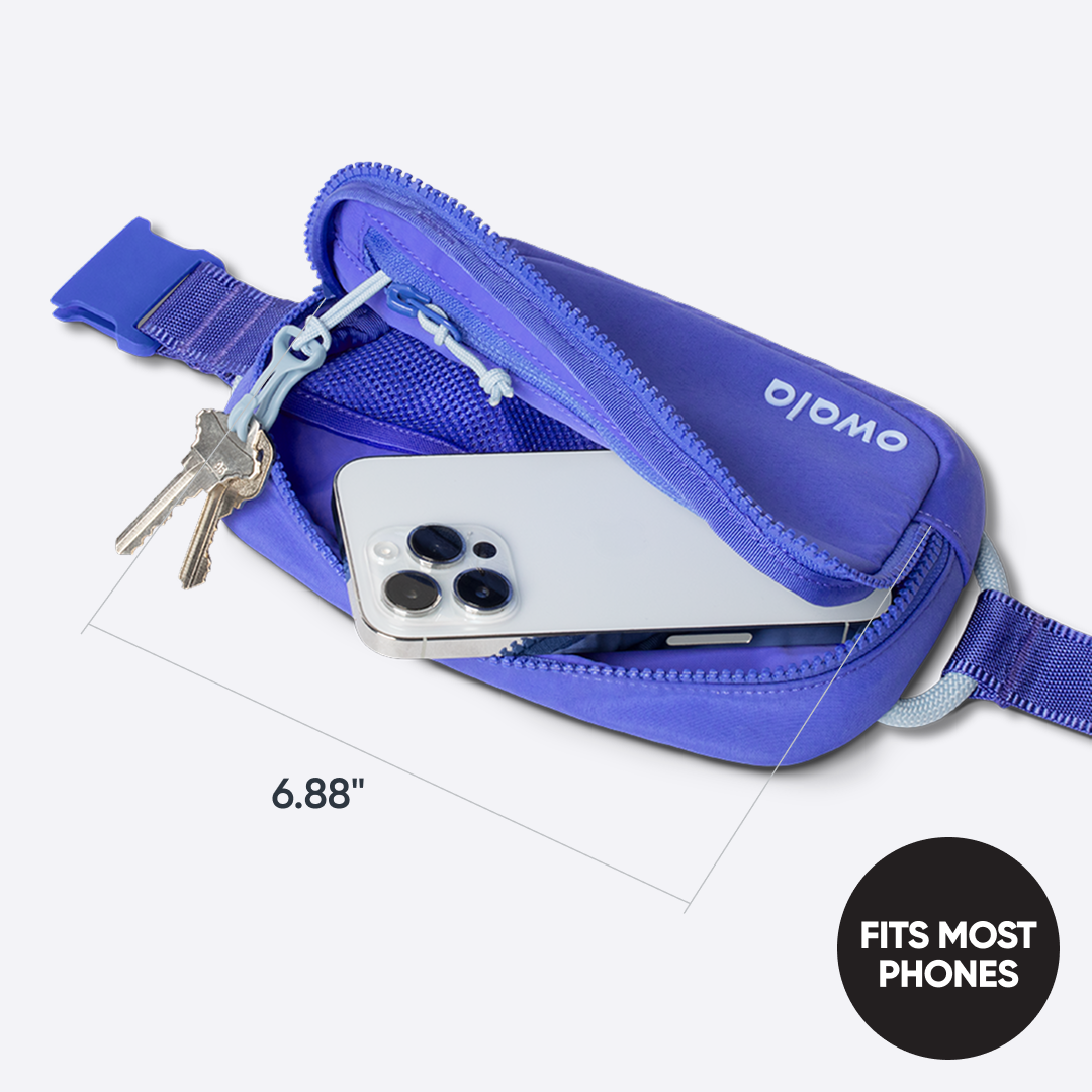 Owala Daily Crossbody in Rest Azured, periwinkle blue belt bag shown open with a smartphone and keys inside, dimensioned at 6.88 inches wide, with badge reading "FITS MOST PHONES"