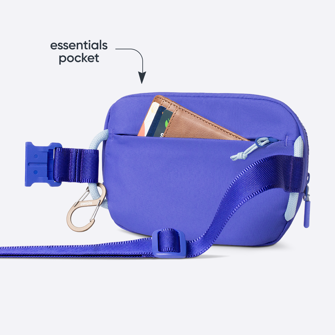Owala Daily Crossbody in Al Fresco, peach belt bag with matching strap, buckle, carabiner, and zipper, shown from the back with a brown leather card wallet tucked into the rear zip pocket, with text reading "essentials pocket"