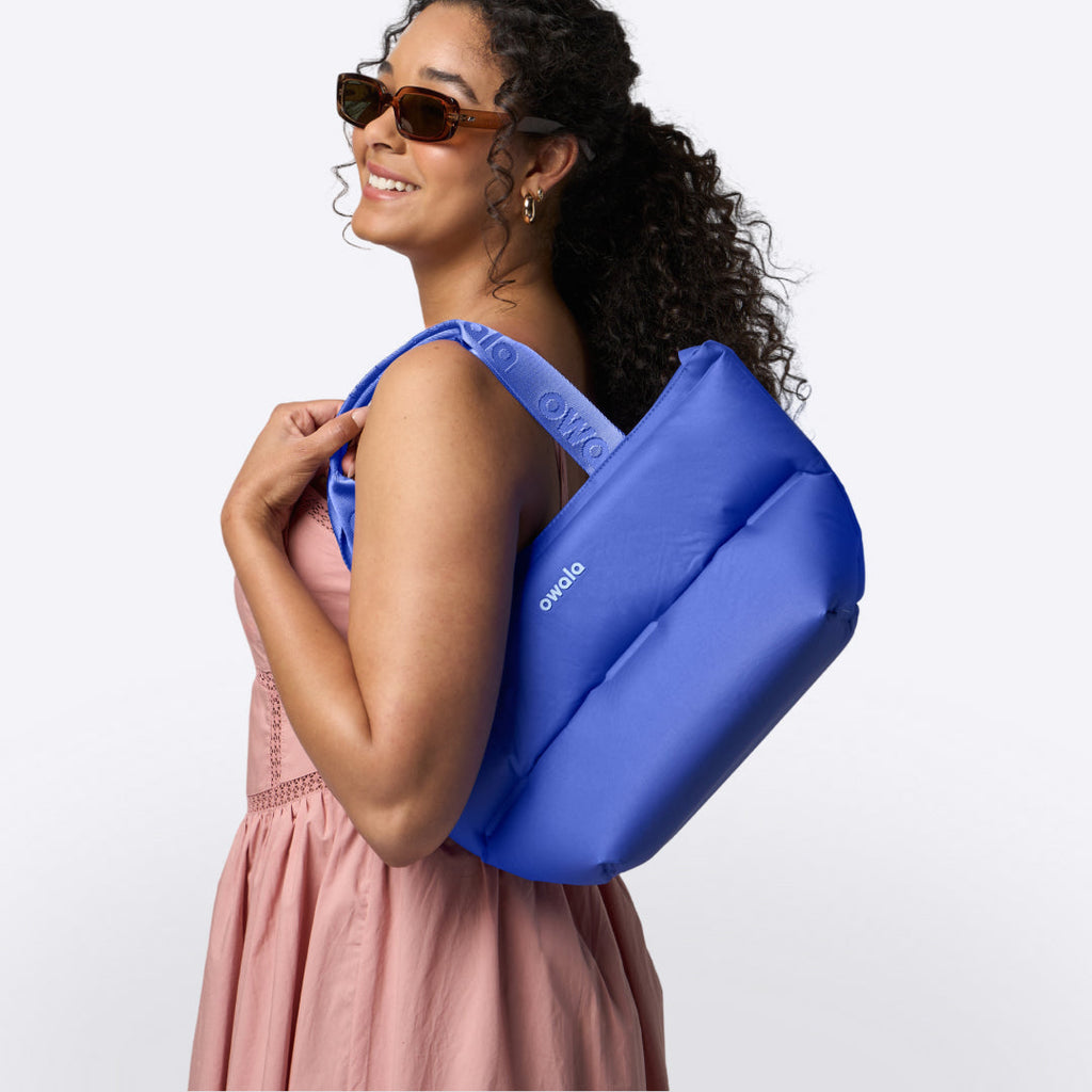 Owala Puffer Mini in Al Fresco, cobalt blue puffy tote with matching owala-branded handles worn over the shoulder of a woman in sunglasses and a pink dress