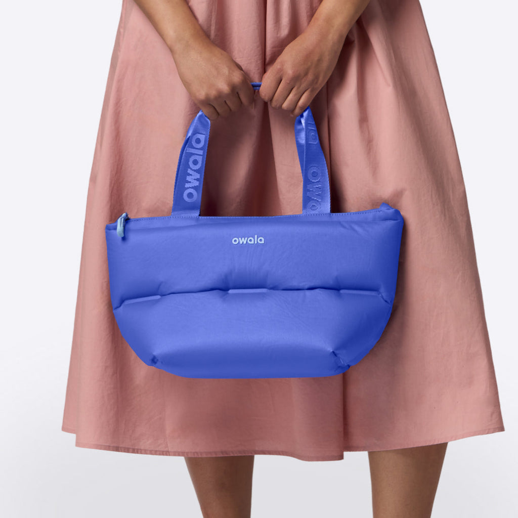 Owala Puffer Mini in Al Fresco, cobalt blue puffy tote with matching owala-branded handles held in front of a woman in a pink dress