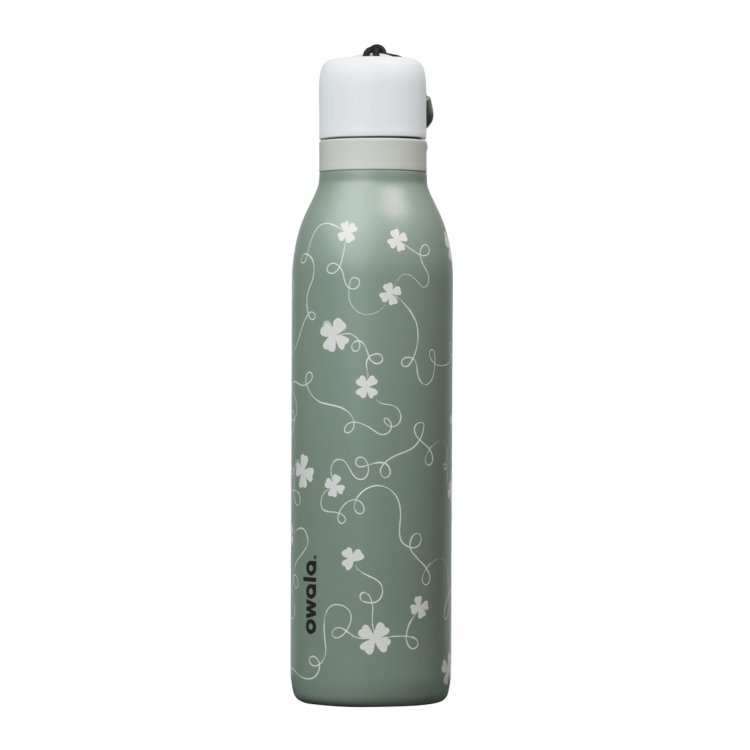 Owala FreeSip Twist 24oz in Clover Achiever, close-up of the sage green body with white clover and vine pattern and the white twist cap with sage carry string and dark carry string grip