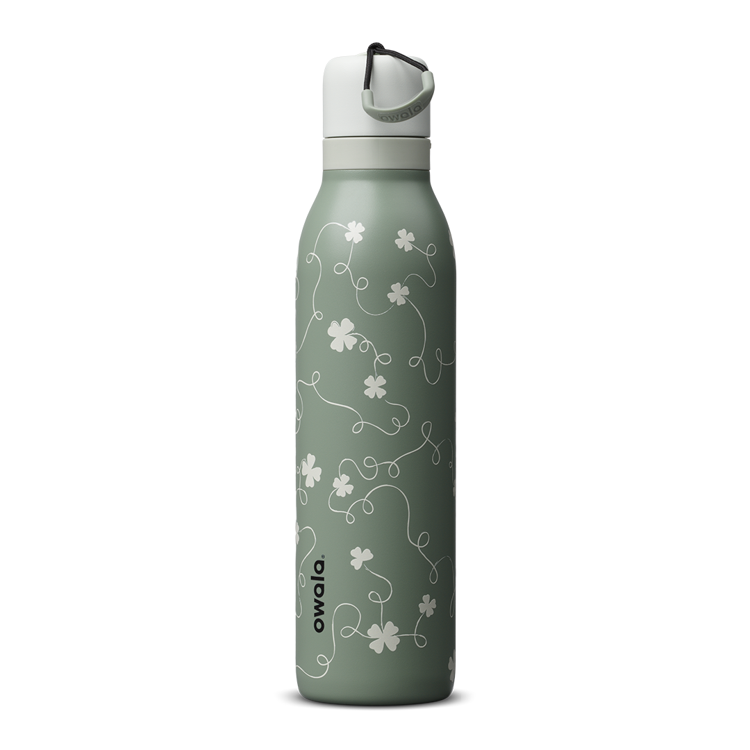 Owala FreeSip Twist 24oz in Clover Achiever, sage green insulated stainless steel body with white clover and vine Color Drop pattern, white twist cap with sage carry string and dark carry string grip