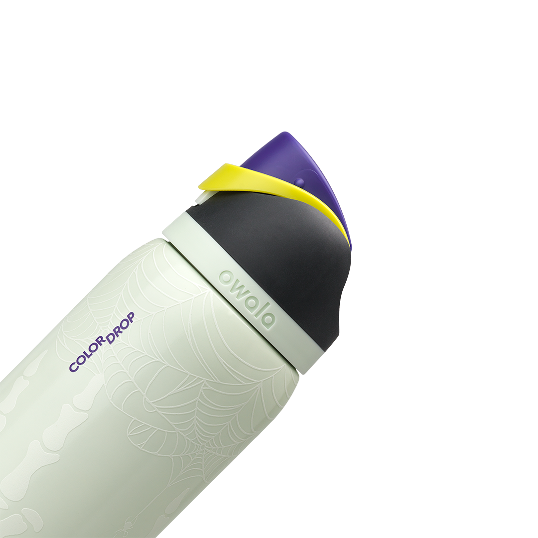 Owala FreeSip 32oz in RIP, pale mint insulated stainless steel body with "COLOR DROP" print and skeleton glow detail, flip cap closed with black lid, purple flip cap and yellow carry loop; glows in the dark