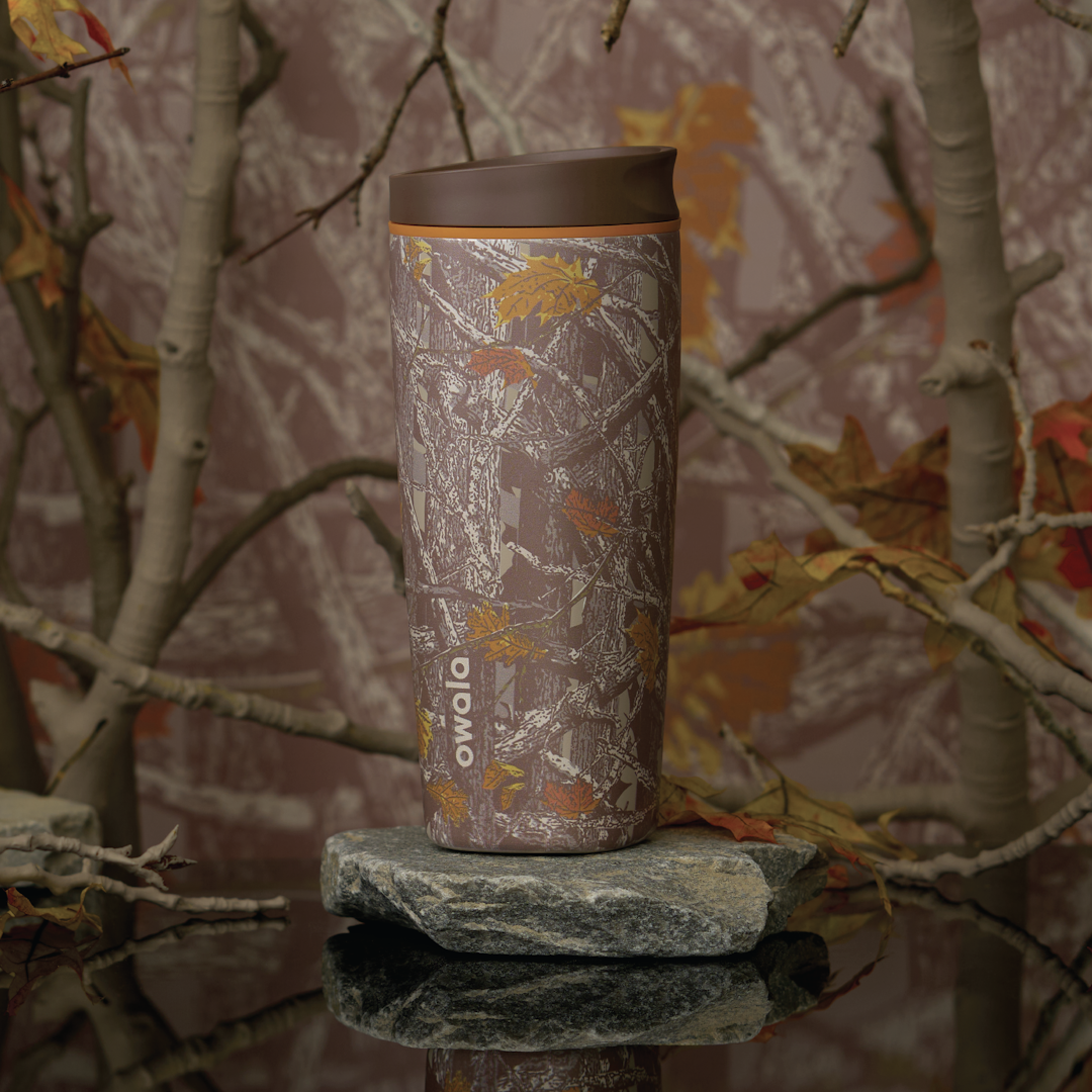 Owala SmoothSip Slider in Out of Sight, woodland camo patterned body in brown and tan with matching brown flip cap and carry loop, shown on a mossy rock against a forest backdrop