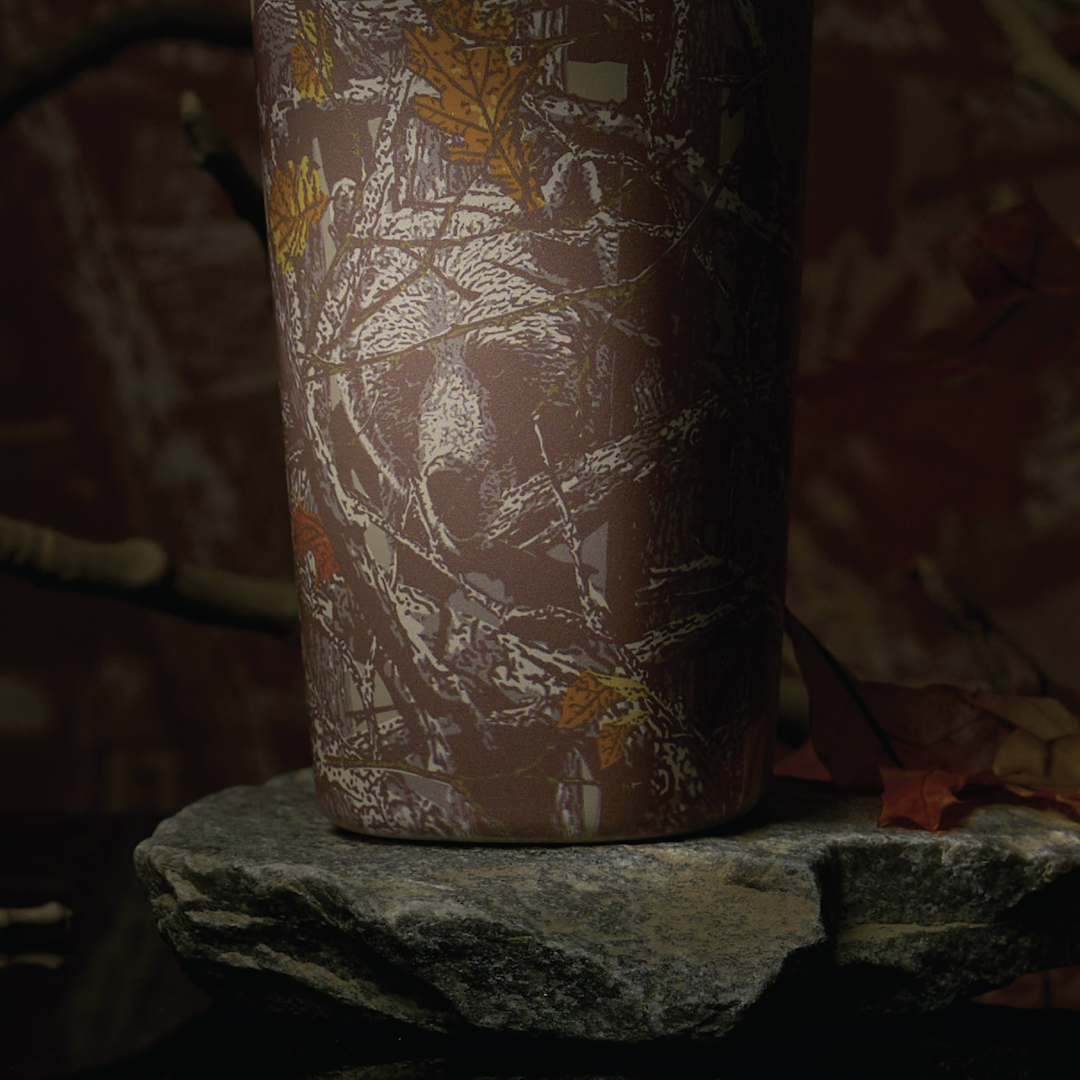 Owala SmoothSip Slider in Out of Sight, back view of woodland camo patterned body shown on a rock in a forest setting